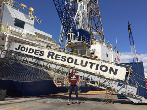 Photo of PhD candidate Adriane Lam standing in front of loading ramp to the ship Joides Resolution. Joides Resolution, in large capital letters adorns the loading ramp