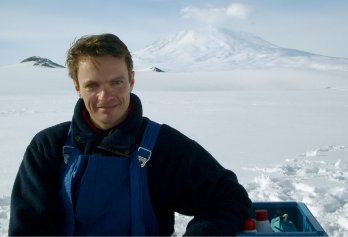 Portrait of Dr. Rob Deconto, smiling at camera in front of white snow field, with volcano in backrgound, in Antarctica